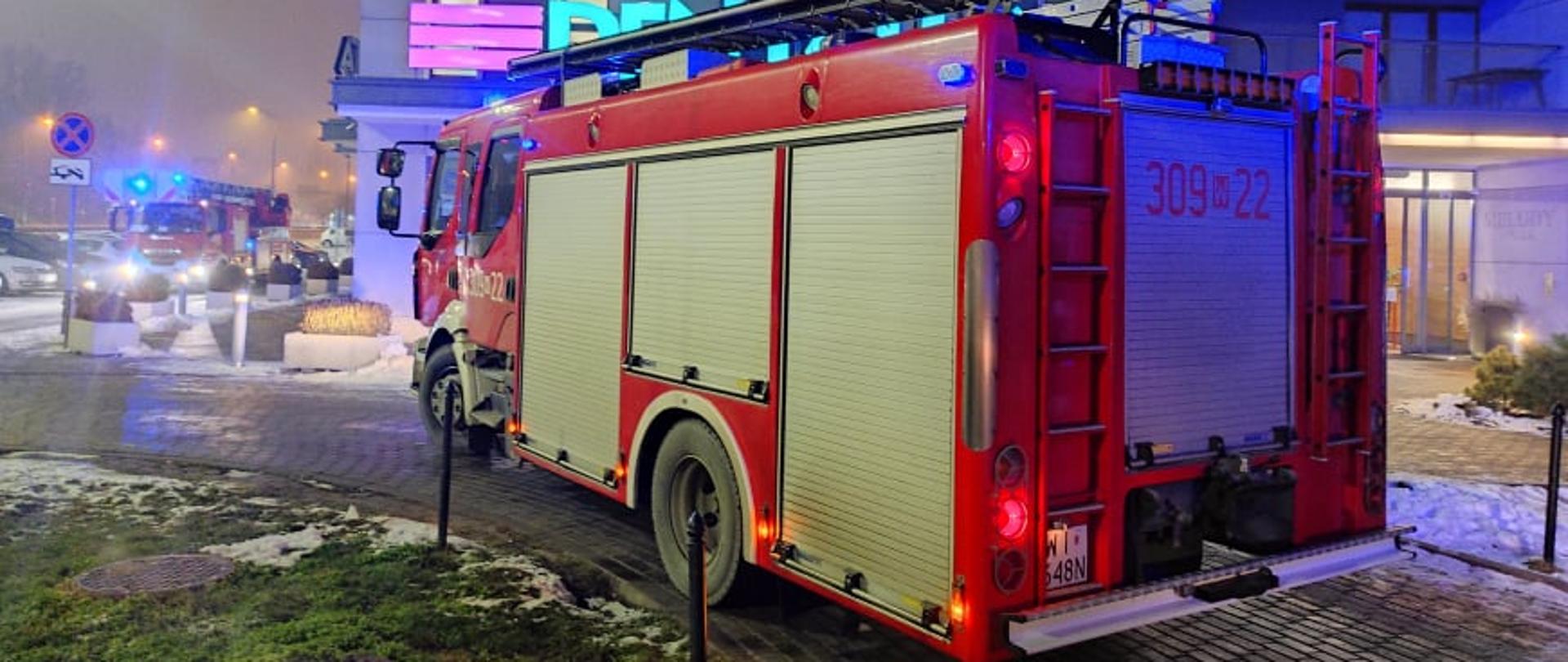 Na zdjęciu widoczny jest budynek w którym miał miejsce pożar samochodu, na pierwszym planie widoczny jest samochód straży pożarnej.