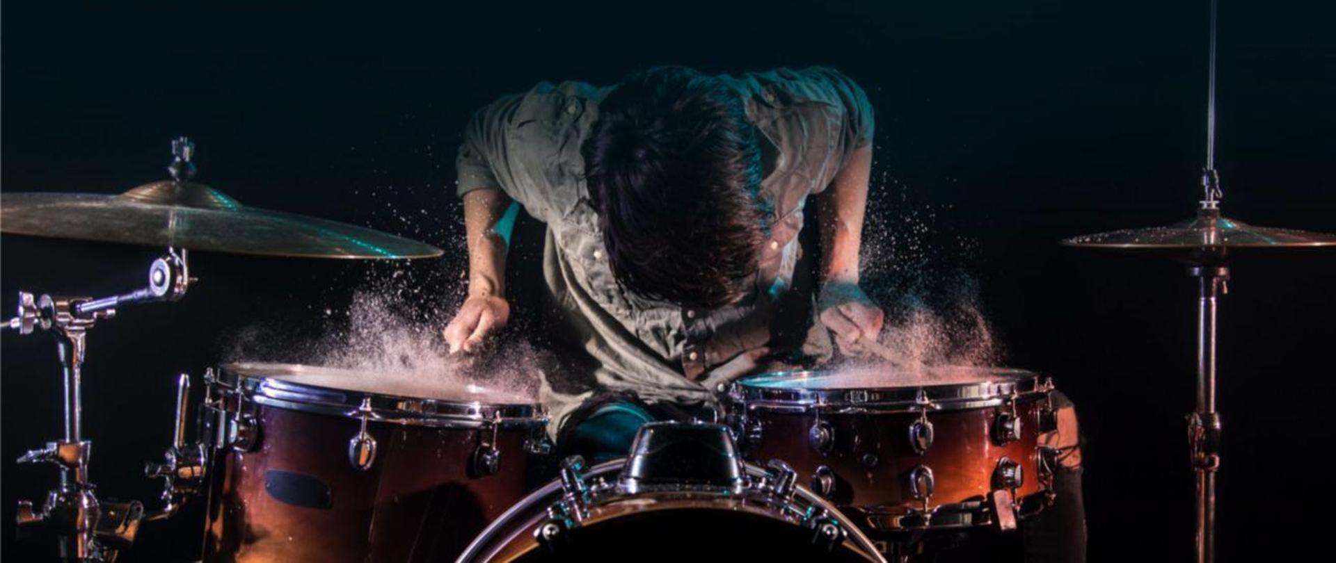 Plakat reklamujący koncert w wykonaniu uczniów klasy perkusji. Na plakacie zdjęcie osoby grającej na zestawie perkusyjnym na ciemnym tle.