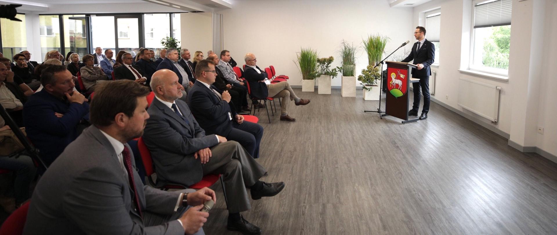 na sali siedzą uczestnicy spotkania i patrzą w kierunku wiceministra Waldemara Budy, który mówi do mikrofonu stojąc za pulpitem 