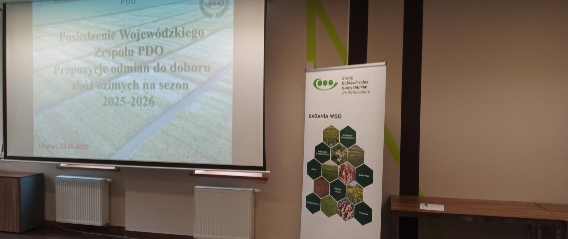 Część sali wykładowej, widać ekran z wyświetlonym slajdem tytułowym: Posiedzenie wojewódzkiego Zespołu PDO, po prawej baner SDOO we Wrócikowie