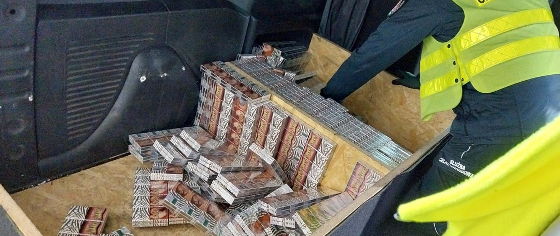 Funkcjonariusz wyjmuje papierosy ze skrytki w aucie