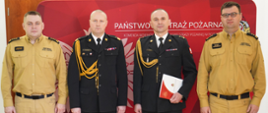 Funkcjonariusze Państwowej Straży Pożarnej w umundurowaniu na czerwonym tle z wizerunkiem godła państwowego.