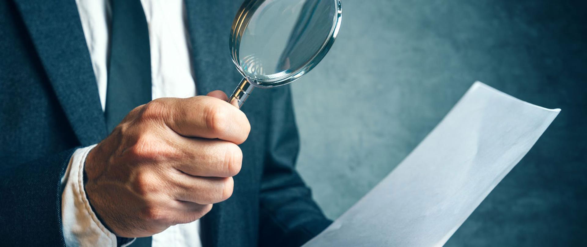 Lupa w dłoni nad dokumentem.