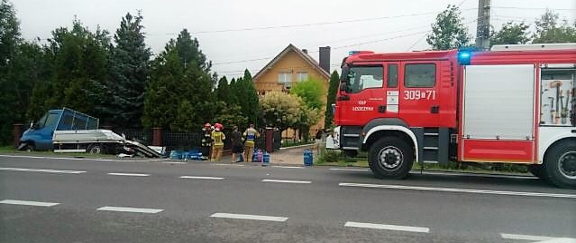 Zdjęcie przedstawia po lewej stronie samochód dostawczy, z którego wysypały się butle LPG – stoją obok samochodu. Z prawej strony stoi samochód pożarniczy a miedzy autami grupa strażaków.