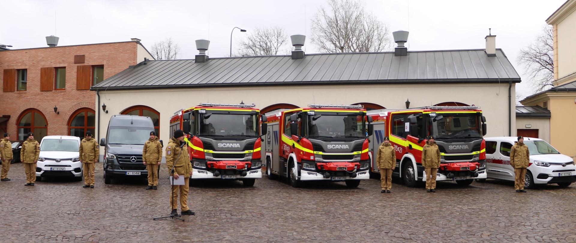 Komendant wita gości na tle nowych samochodów.