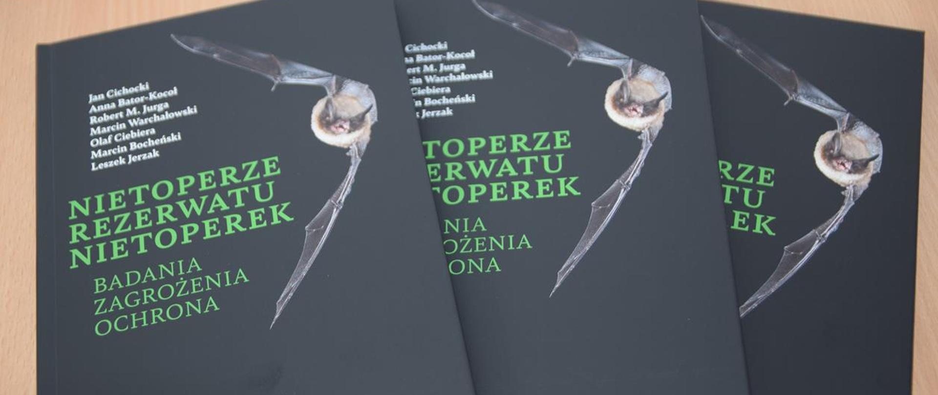 Na zdjęciu trzy książki o tytule Nietoperze Rezerwatu Nietoperek Badania Zagrożenia Ochrona, na nich nietoperz