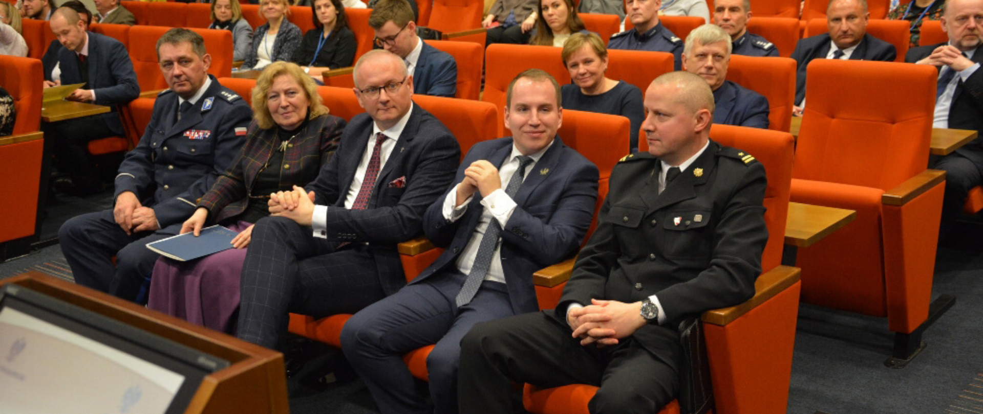 Sala obrad. Ujęcie w stronę siedzisk, w pierwszym rzędzie siedzi minister Adam Andruszkiewicz, obok siedzą między innymi przedstawiciele policji, straży pożarnej, wojewoda wielkopolski