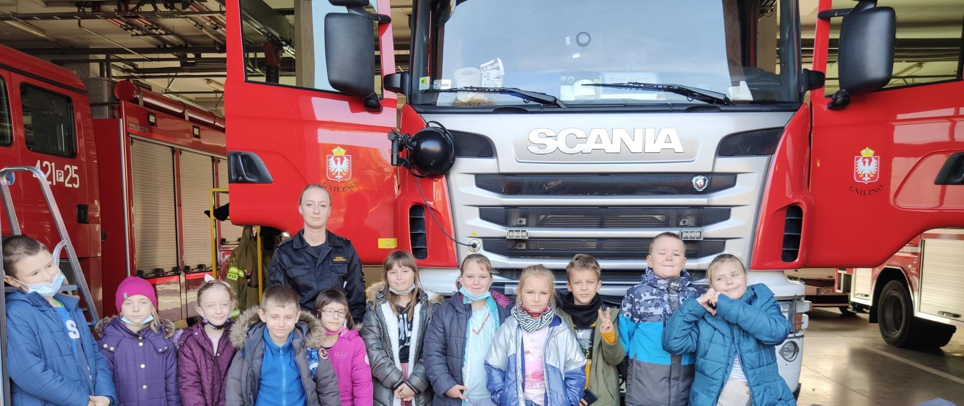 Zdjęcie grupy szkolnej z funkcjonariuszką PSP na tle samochodu strażackiego