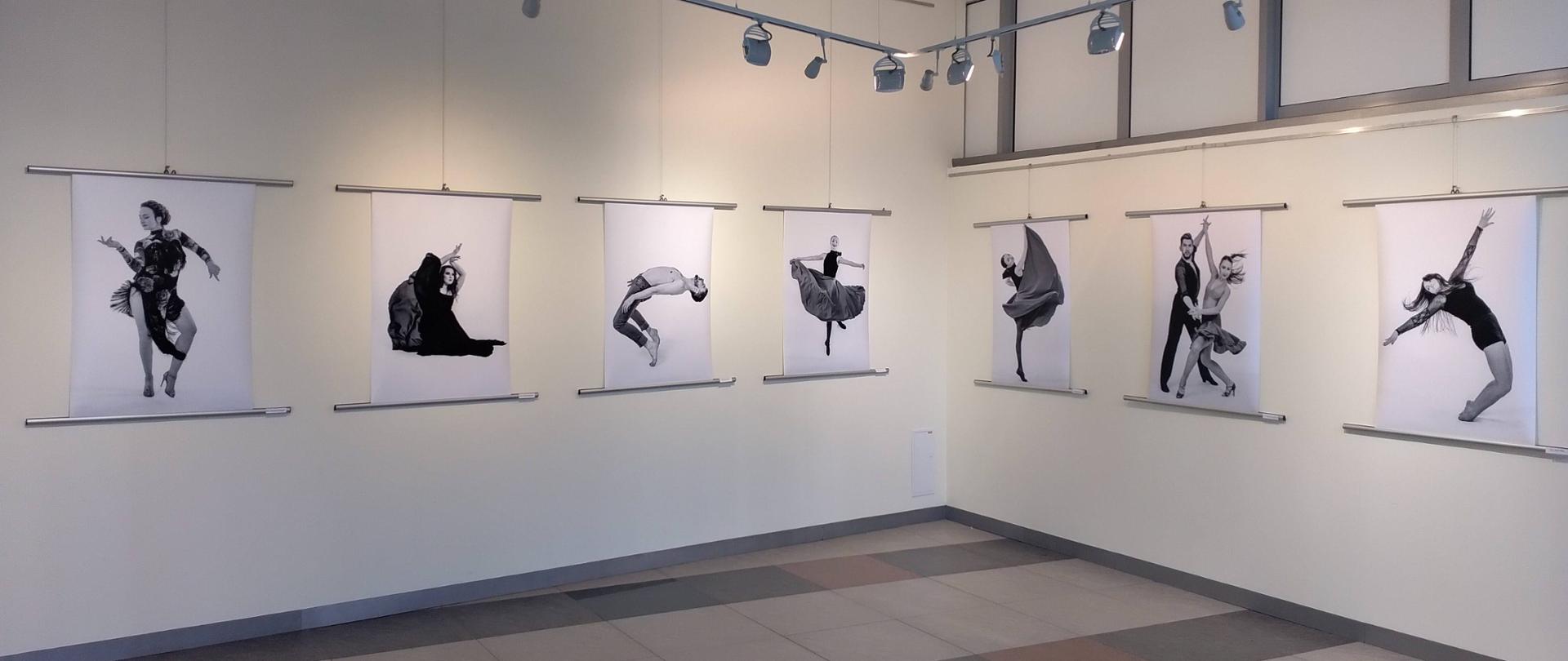 Na białej ścianie wiszą zdjęcia z wystawy fotograficznej "Taniec obrazów - obraz tańca".