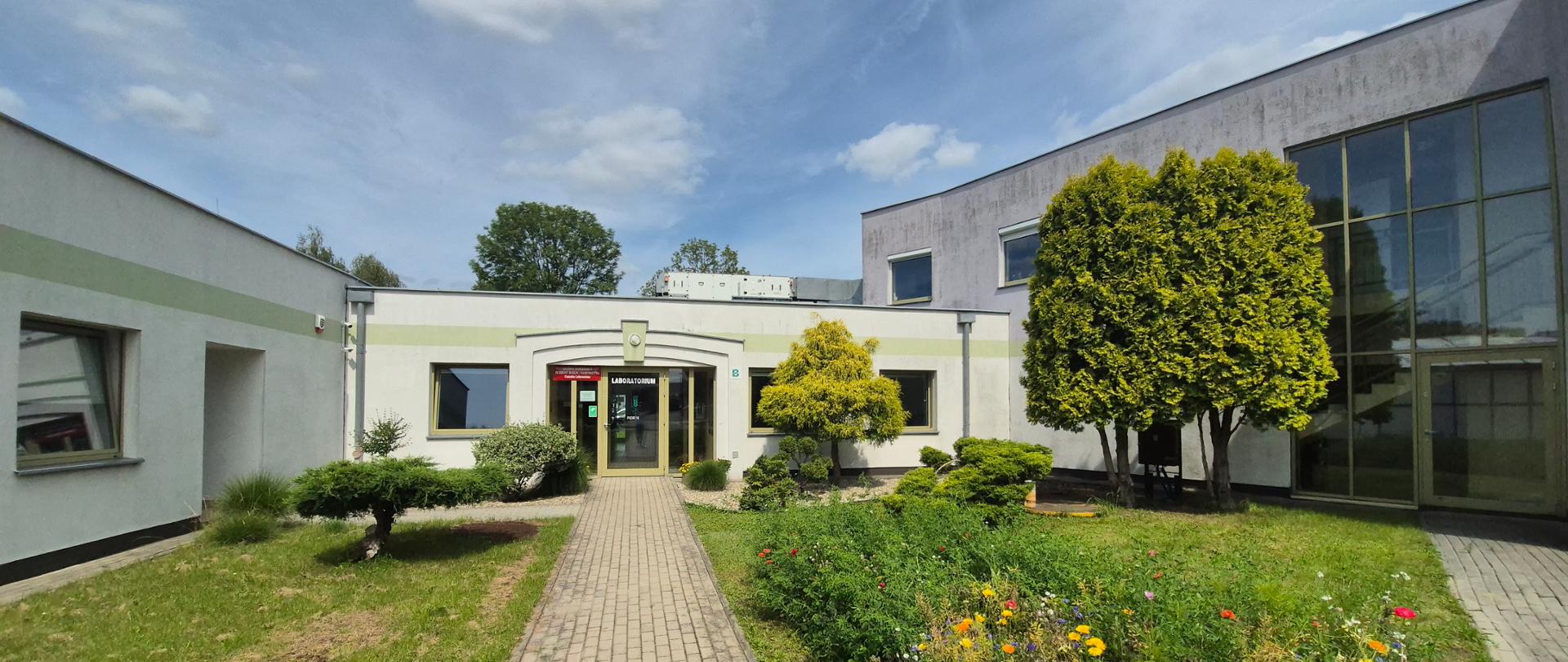 Budynek OCL w Rzeszowie od strony wejścia. Przed budynkiem znajduje się ogród z wytyczonymi chodnikami. 