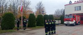 plac zewnętrzny komendy powiatowej, na pierwszym planie masz , połowie masztu wciągana plaga państwowa. Strażacy stoją w szeregu oddają hołd fladze. salutują