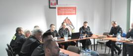 Uczestnicy narady – strażacy PSP w sali konferencyjnej prowadzą ożywioną konwersację.