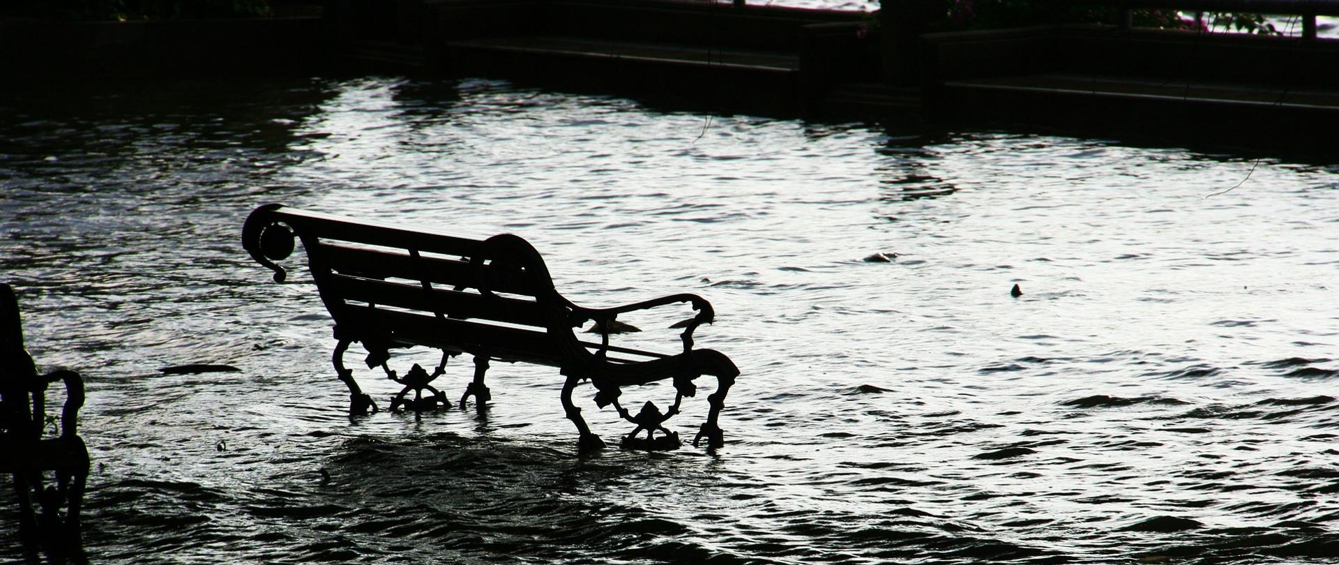 Grafika przedstawia ławkę otoczoną wodą.