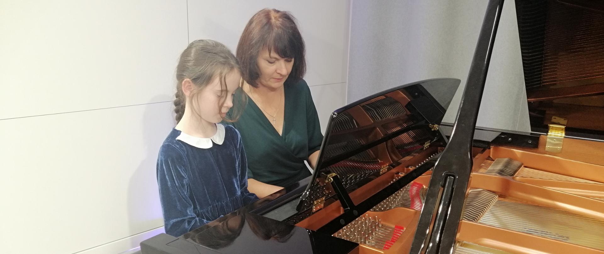 Uczennica w duecie z pedagogiem gra na fortepianie.