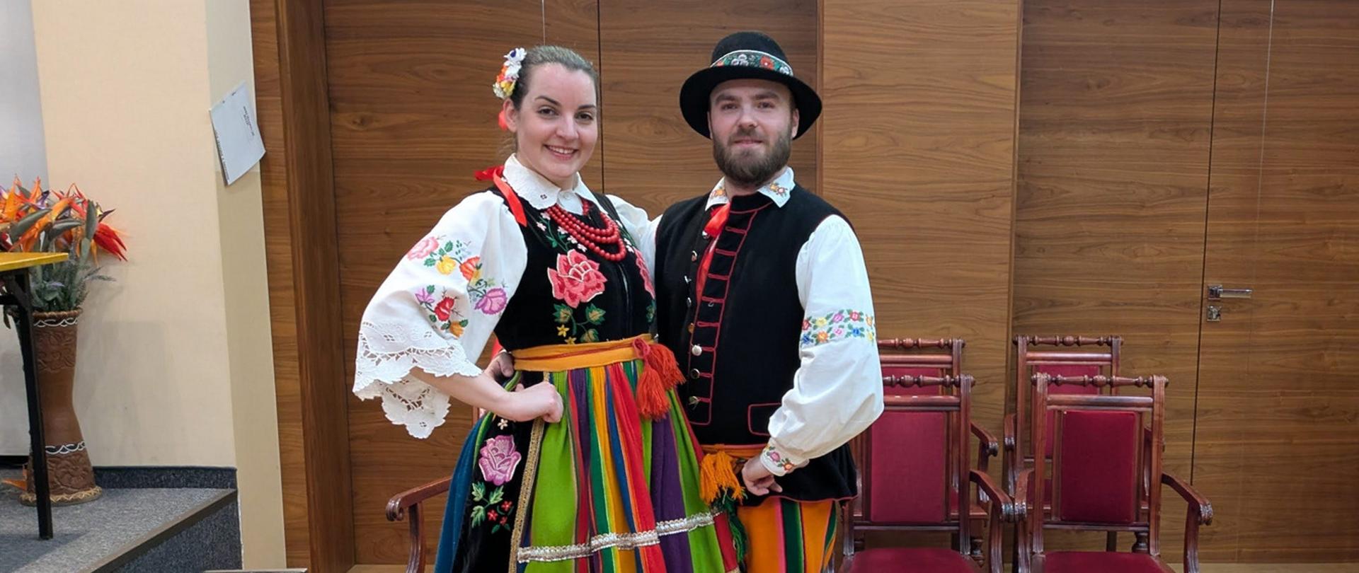 Kobieta i mężczyzna w strojach łowickich stoją obok siebie.