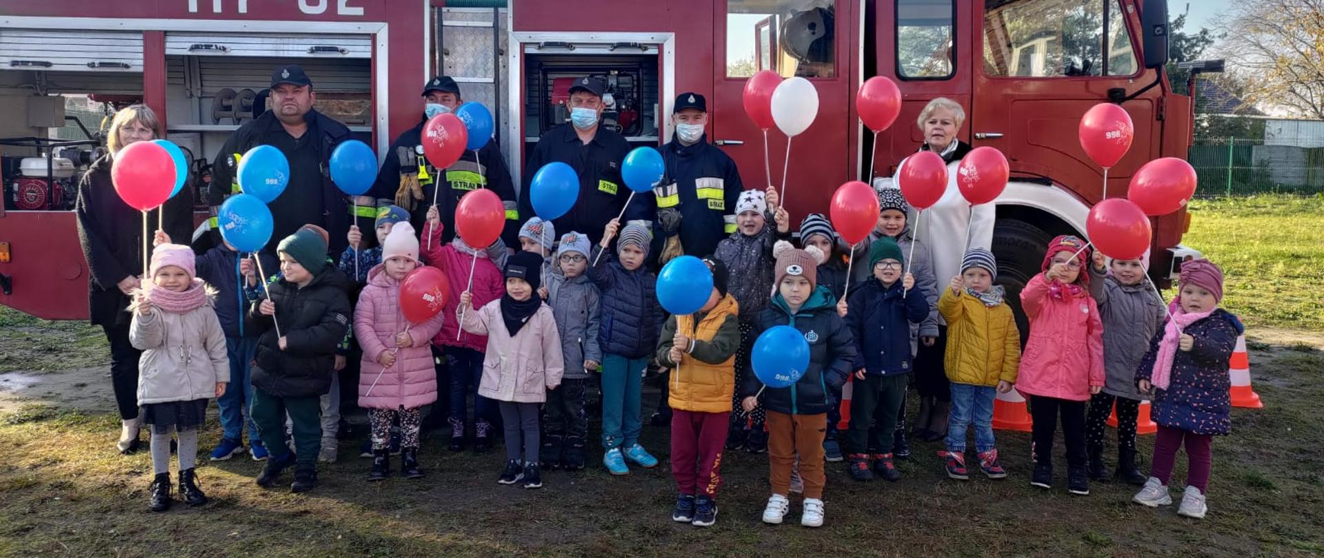 Wspólne zdjęcie dzieci i strażaków przed wozem strażackim.