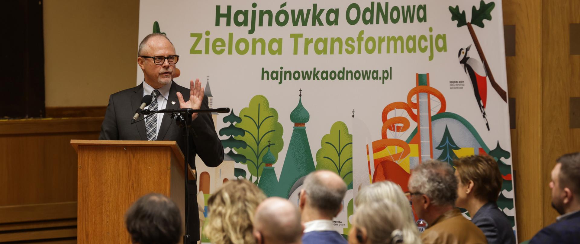 Wiceminister Jacek Protas w mównicy. Przed nim publiczność na krzesłach.