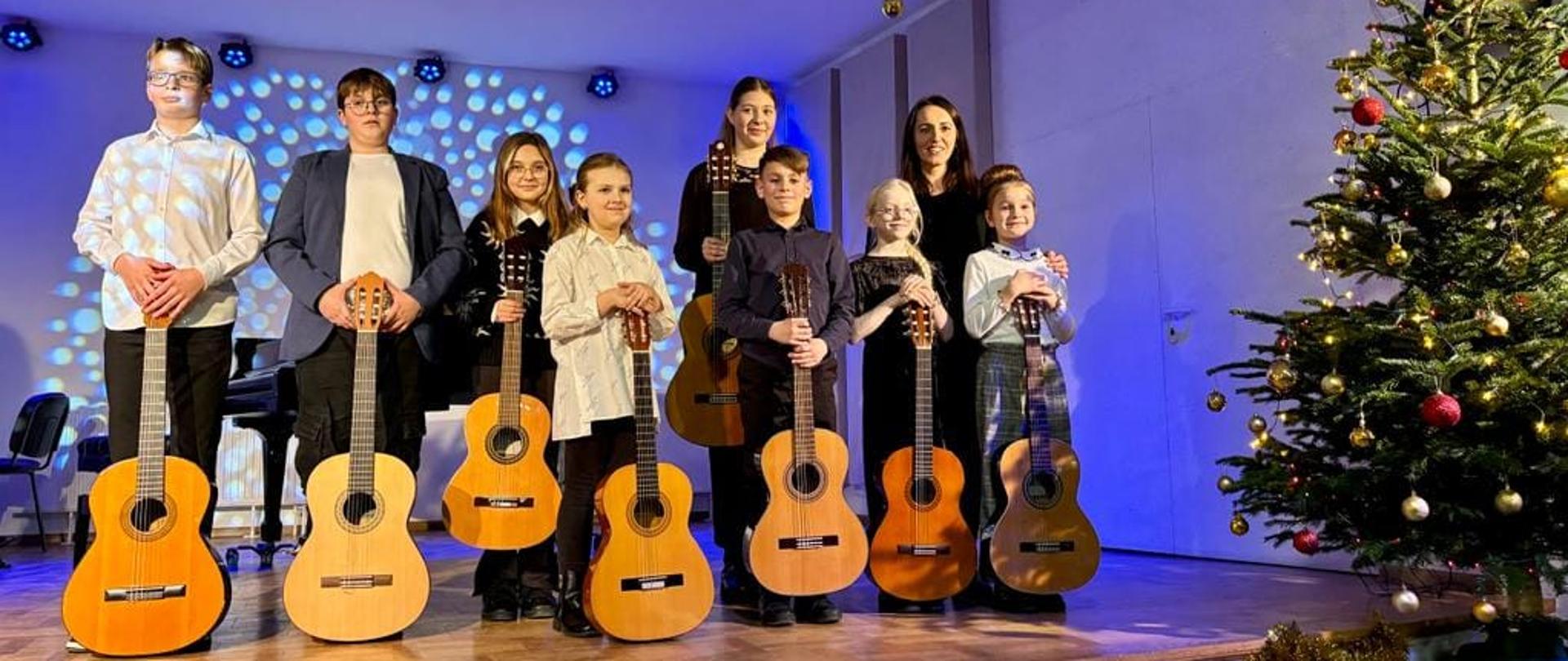 Uczniowie klasy gitary na scenie szkolnej po zakończonej audycji. 
