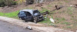 Rozbity samochód osobowy na poboczu jezdni, oparty o słup telekomunikacyjny