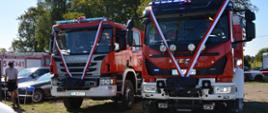 dwa samochody ratowniczo-gaśnicze ozdobione białoczerwonymi wstęgami