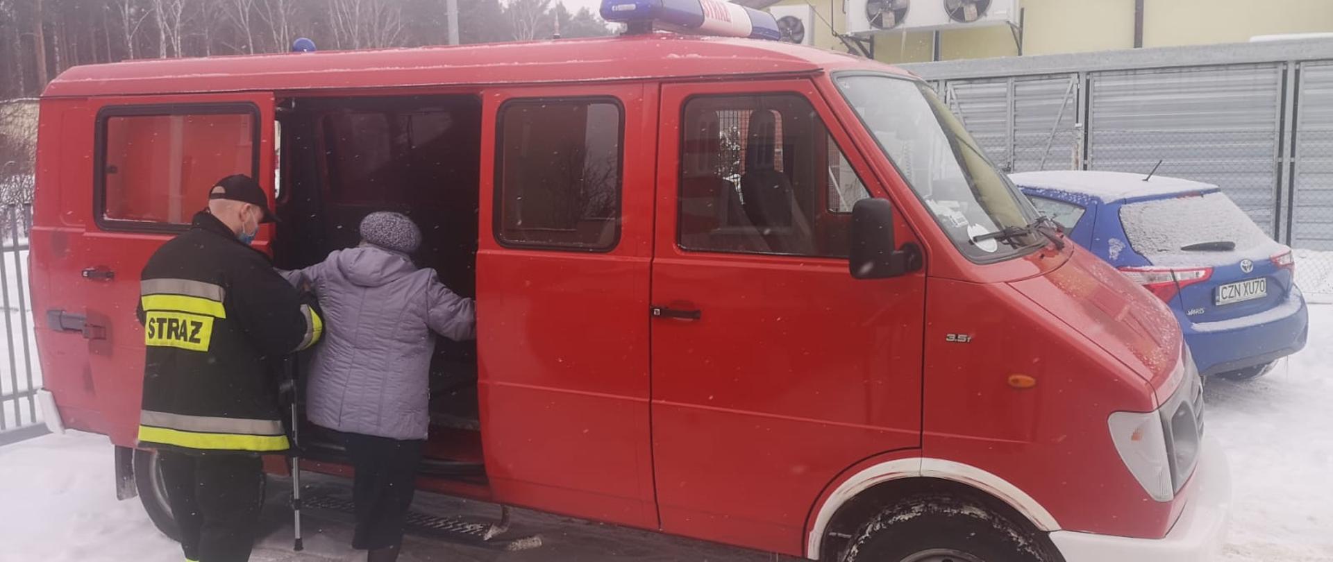 zdjęcie przedstawia strażaka ochotnika OSP Piechcin pomagającego starszej pani wejść do samochodu 