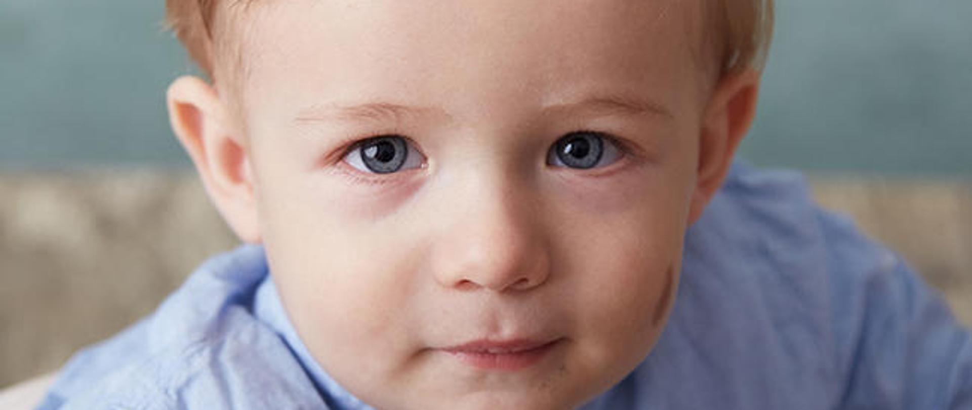 Niespełna 2 – letni chłopiec z lekkim uśmiechem na buzi