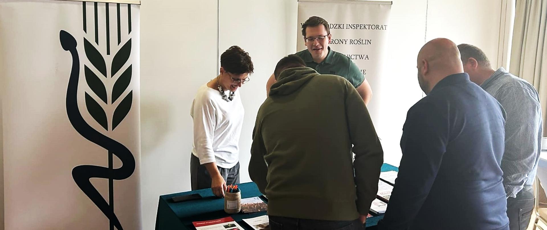 Na zdjęciu stoisko Wojewódzkiego Inspektoratu Ochrony Roślin i Nasiennictwa. Dwóch przedstawicieli rozmawia z trzema zainteresowanymi osobami, które oglądają materiały informacyjne na stole. W tle widoczne są roll-upy z logo PIORiN