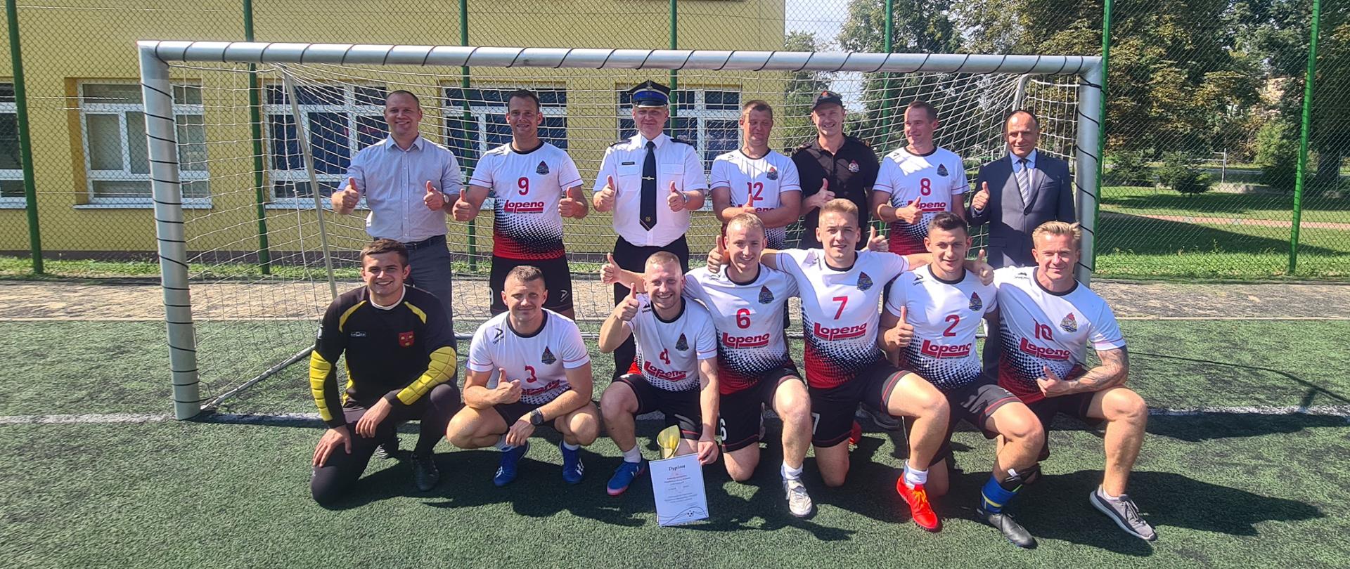 zwycięska drużyna z zaproszonymi gośćmi stoją na tle bramki piłkarskiej 