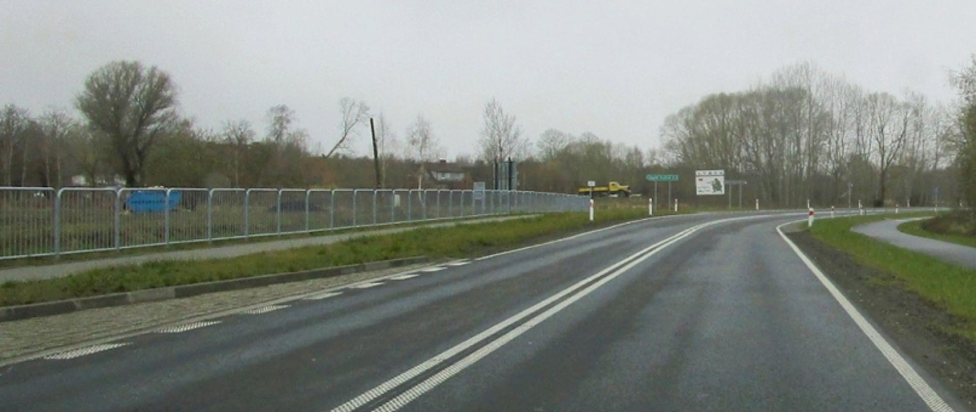 Na zdjęciu widać pusta drogę. Po obu jej stronach znajduje się chodnik dla pieszych.