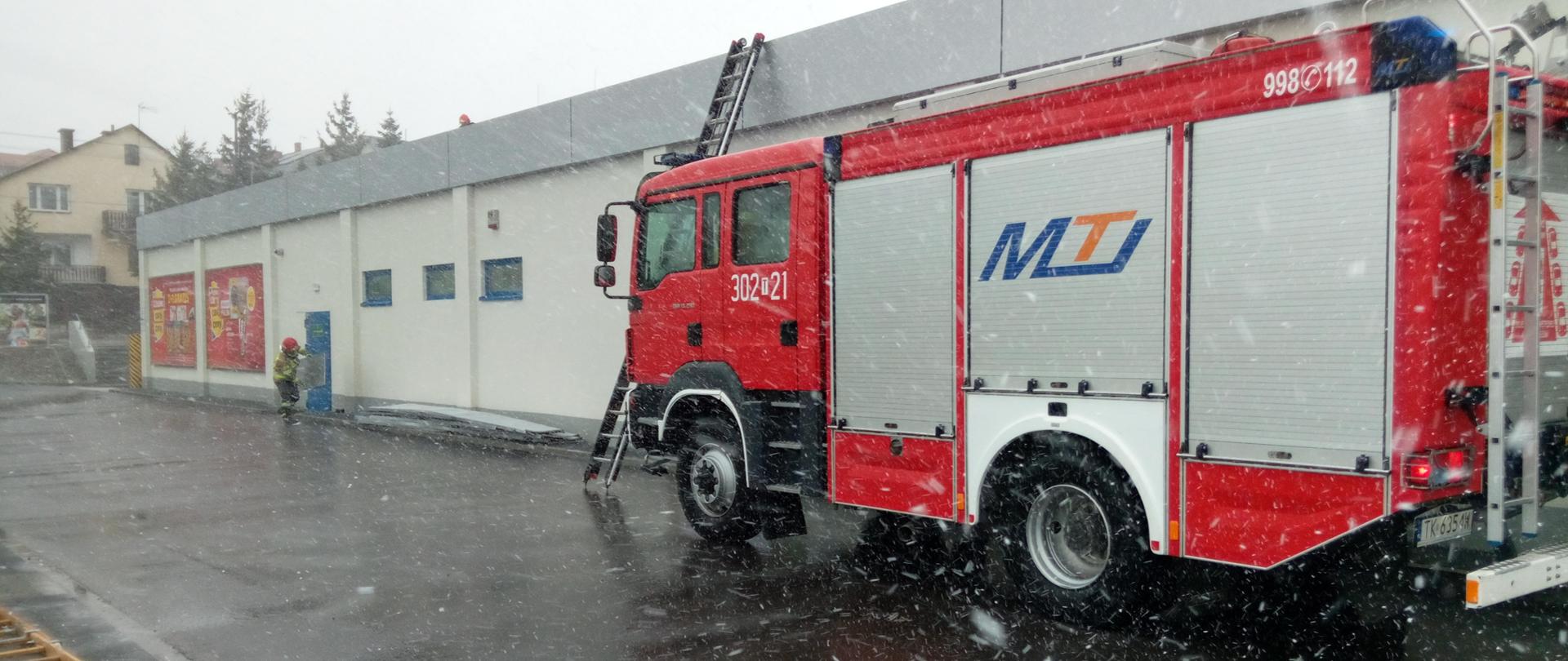 Na zdjęciu widzimy samochód pożarniczy na tle budynku handlowego, gdzie usuwana była naderwana przez silny wiatr obróbka blacharska na długości 70 m