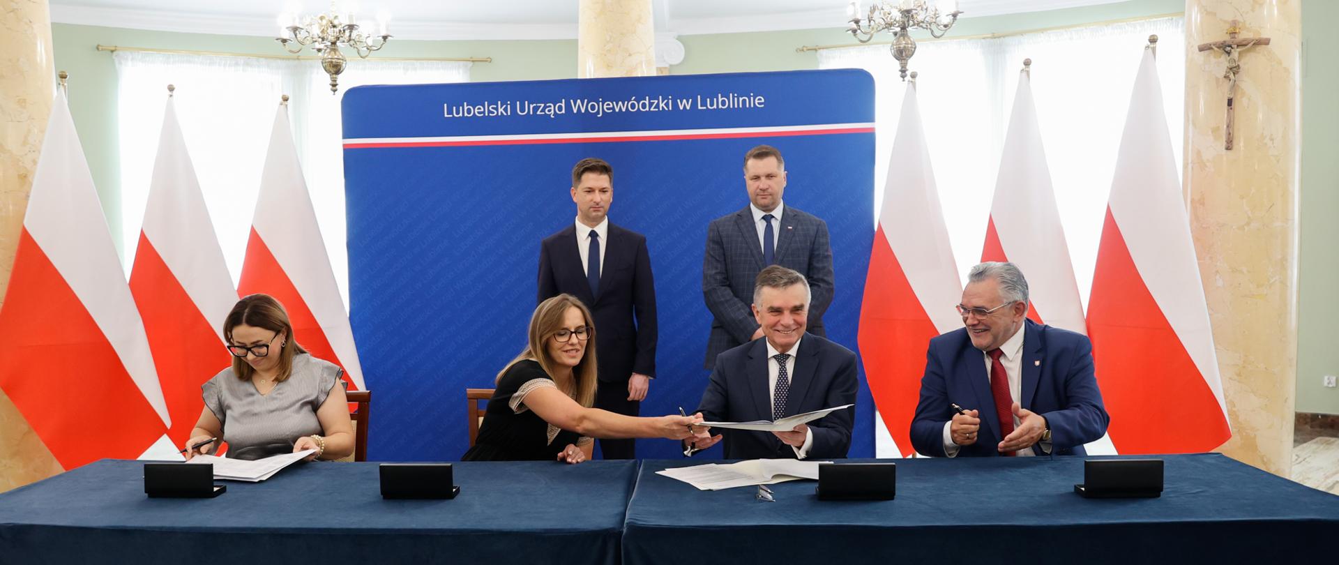 Mężczyźni i kobiety siedzą za stołem i podpisują umowy.