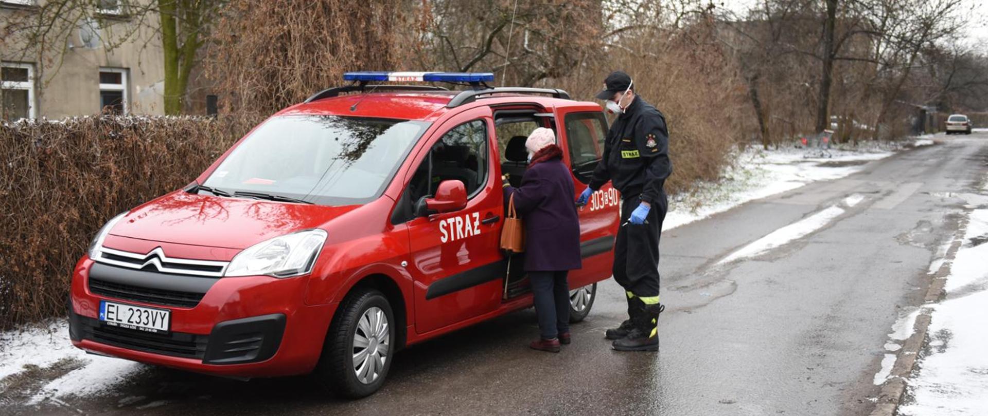 Na zdjęciu strażak pomagający wsiąść do samochodu starszej osobie transportowanej na szczepienie.