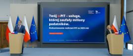 Dwie osoby stoją przy oddzielnych mównicach, a między nimi ekran z napisem „Twój e‑PIT – usługa, której zaufały miliony podatników” oraz informacją o podsumowaniu PIT za 2025 rok.