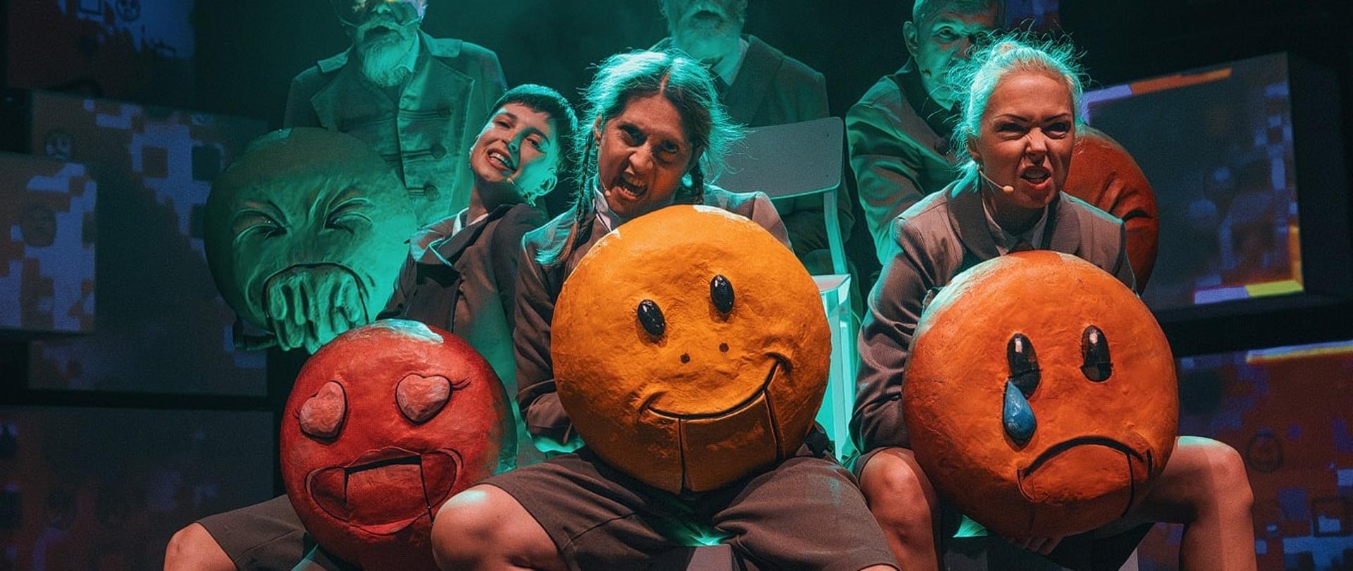 3 osoby z różnymi minami trzymają czerwone, żółte i pomarańczowe duże krążki symbolizujące emotikony