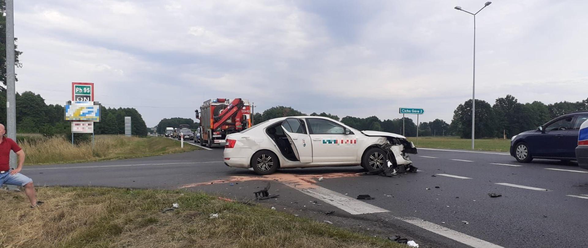 Dzień. Na skrzyżowaniu stoi uszkodzony samochód, w tle samochód ratownictwa technicznego z JRG Nowy Tomyśl.