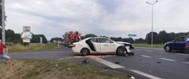 Dzień. Na skrzyżowaniu stoi uszkodzony samochód, w tle samochód ratownictwa technicznego z JRG Nowy Tomyśl.