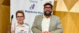 Zdjęcie saksofonisty z nauczycielem na tle banera PSM