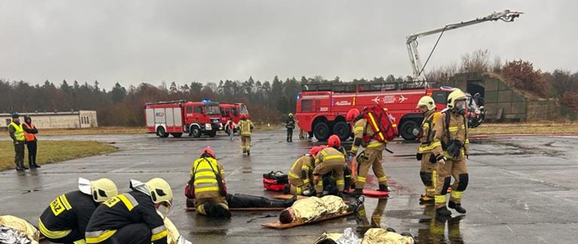 Strażacy udzielający pomocy osobom poszkodowanym (pozorantom ćwiczeń)