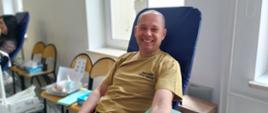 Na zajęciu widoczny strażak w koszulce i spodniach koloru piaskowego siedzący na fotelu na sali oddający krew podczas akcji zbiórki krwi zorganizowanej przez Klub Honorowych Dawców Krwi Polskiego Czerwonego Krzyża przy Komendzie Powiatowej Państwowej Straży Pożarnej w Gorlicach 