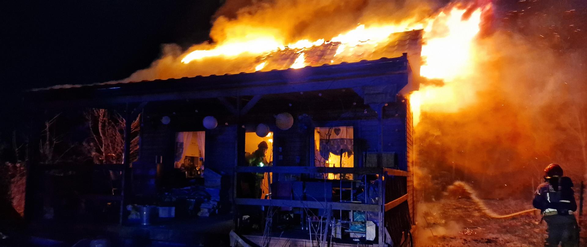 Budynek objęty pożarem obok strażacy podający prądy wody. pora nocna