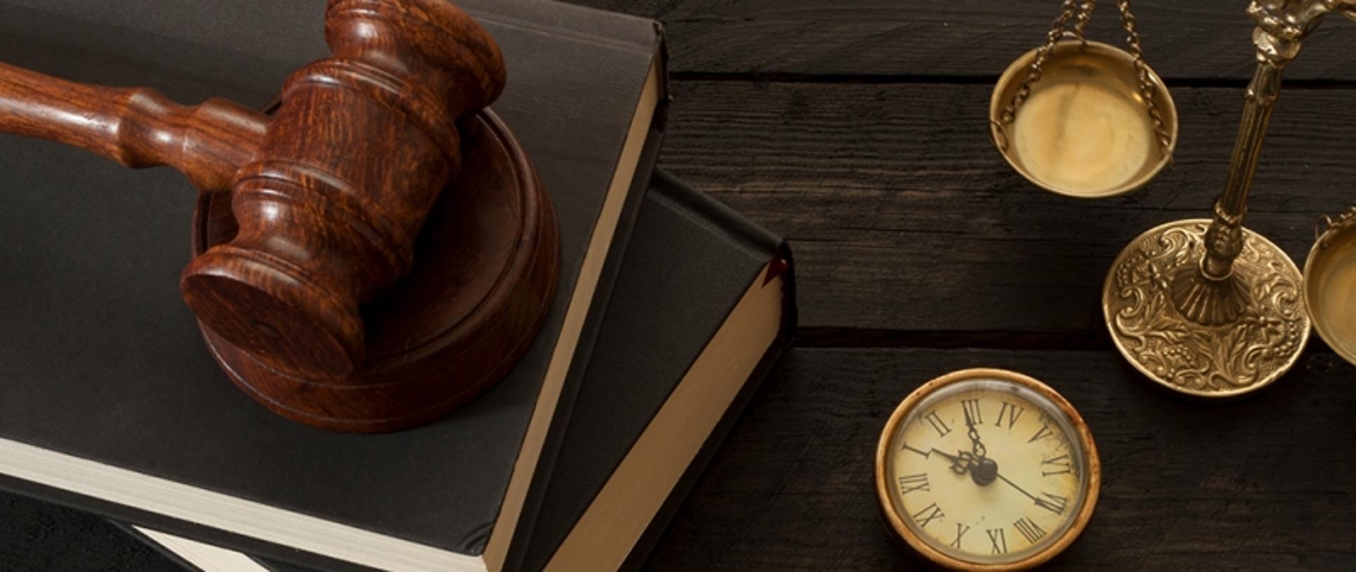 Młotek sędziowski, zegarek kieszonkowy i waga szalkowa na drewnianym tle.