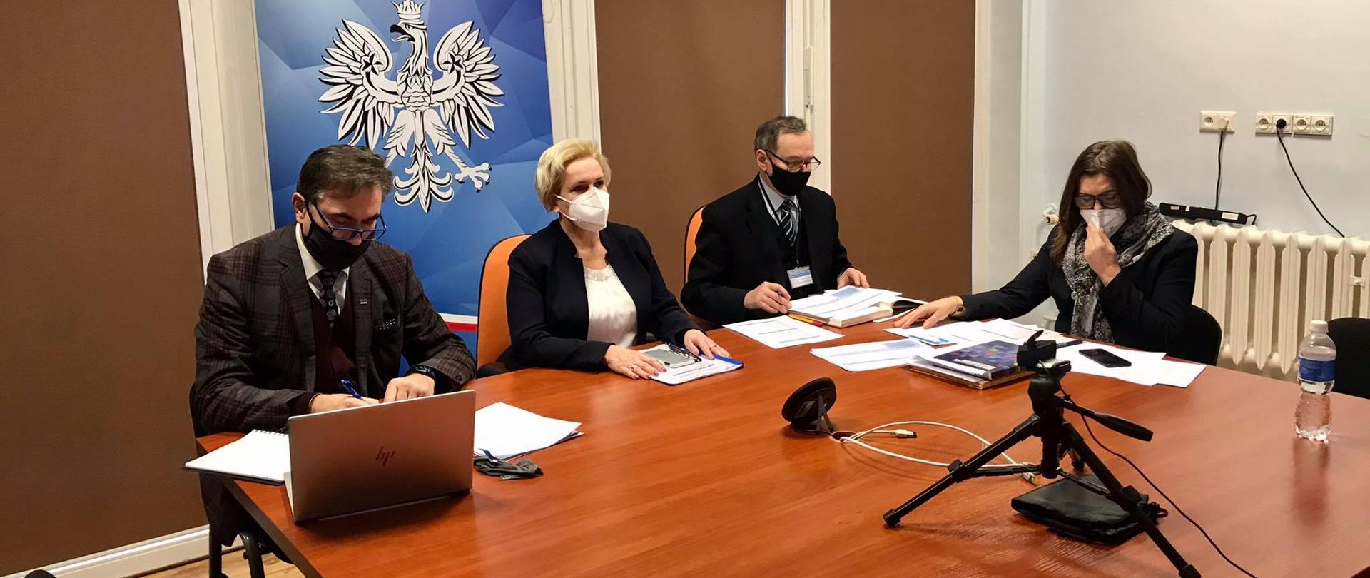 Na zdjęciu cztery osoby, zasiadające za stołem. Po lewej stornie kadru dyrektor OOW NFZ, następnie wicewojewoda opolski oraz dwoje dyrektorów w OUW. Za plecami wicewojewody widać roll up w kolorze błękitnym z napisem wicewojewoda opolski. Dyrektor NFZ, zasiadający po prawej stronie od wicewojewody, notuje na kartkach papieru. Przed nim stoi laptop. Wszyscy na zdjęciu pozostają w skupieniu. Wicewojewoda patrzy centralnie w dal. 