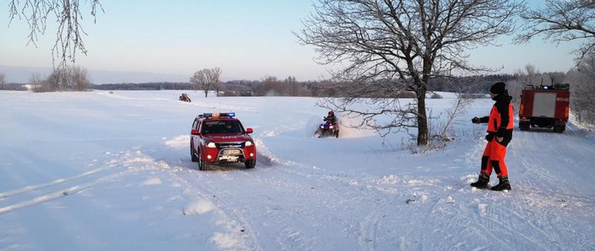 Na zdjęciu widać dwa samochody straży pożarnej oraz quad na gąsienicach użyty podczas dotarcia do osób potrzebujących