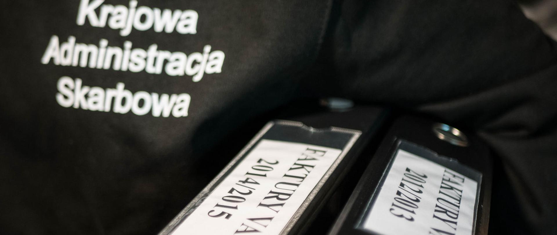 Segregatory z fakturami VAT, trzymane przez funkcjonariusza KAS.