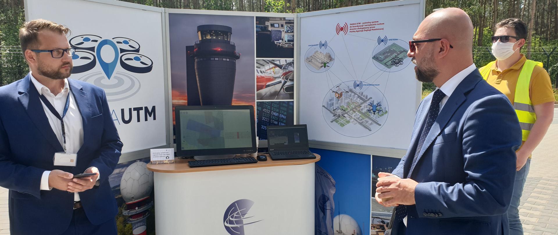 Na zdjęciu widać 3 osoby, które stoją przy makiecie z napisem PANSA UTM. 