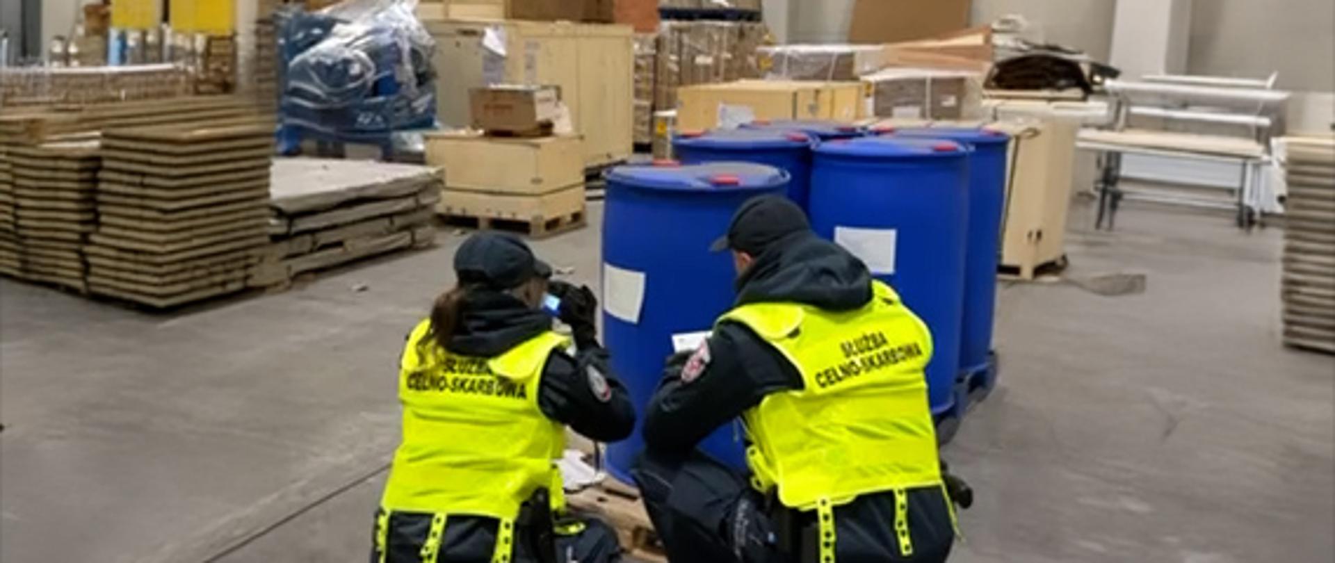 Funkcjonariusze Służby Celno-Skarbowej przy niebieskich beczkach.