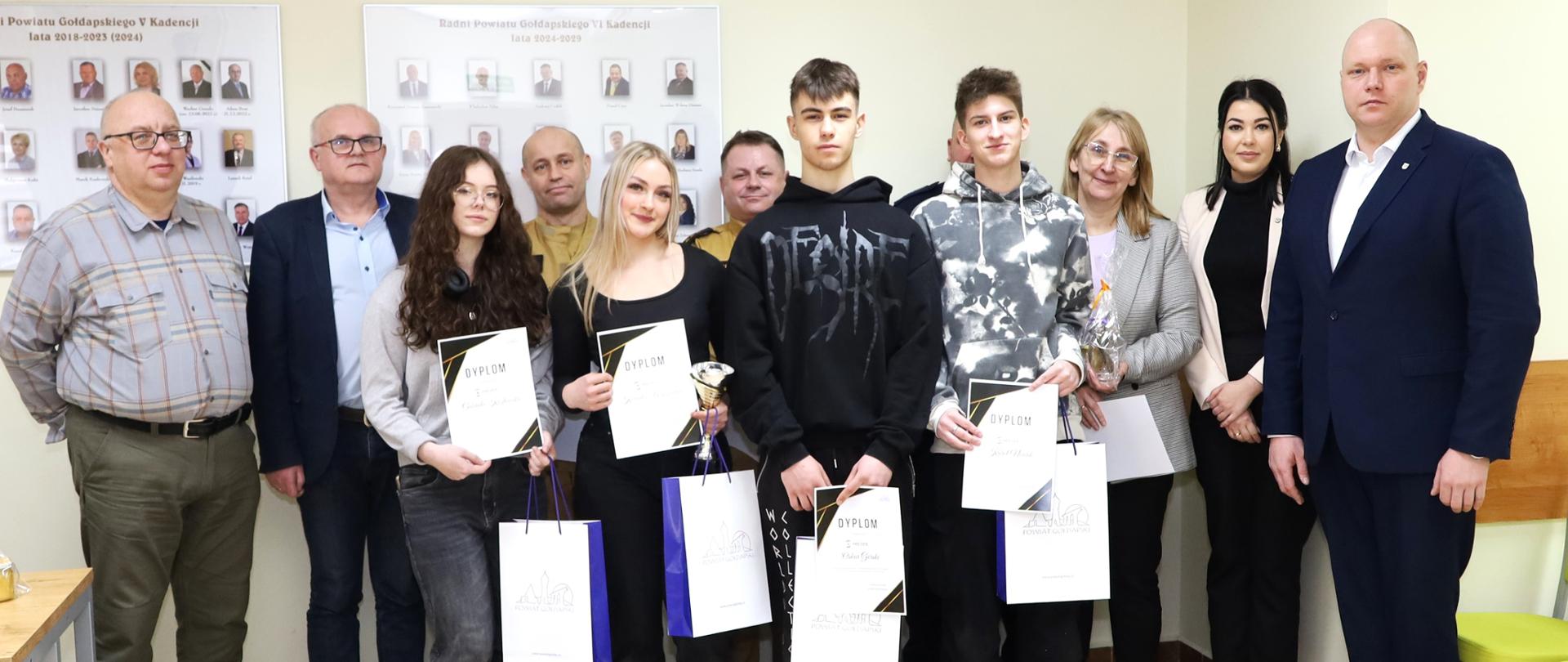 Zdjęcie przedstawia uczestników I Wojewódzkiego Konkursu Wiedzy o Ochronie Ludności i Bezpieczeństwie Powszechnym (eliminacje międzyszkolne) wraz z ich opiekunami oraz przedstawicieli Starostwa Powiatowego w Gołdapi na czele ze Starostą Gołdapskim Panem Krzysztofem Kazanieckim (pierwszy od prawej w pierwszym rzędzie). Na obrazie obecni są również przedstawiciele zespołu sędziowskiego, w tym st. kpt. Bogdan Mielnik oraz st. ogn. Jacek Klimko z Komendy Powiatowej Państwowej Straży Pożarnej w Gołdapi
