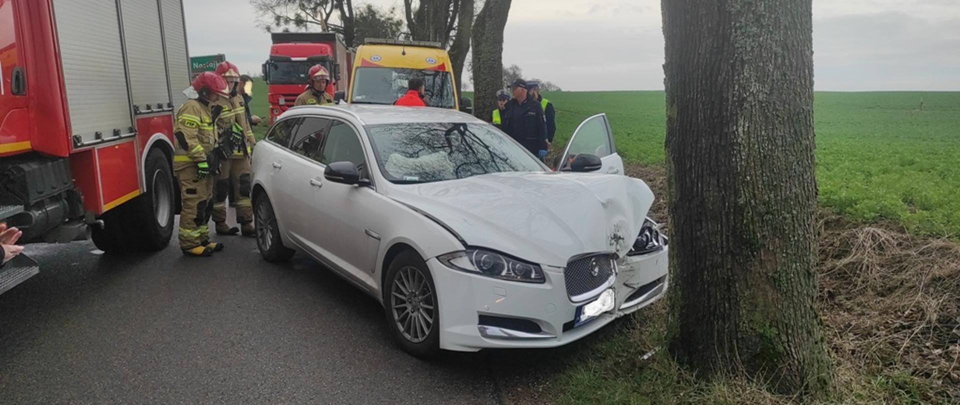 Samochód osobowy stoi na jezdni po uderzeniu w drzewo. 