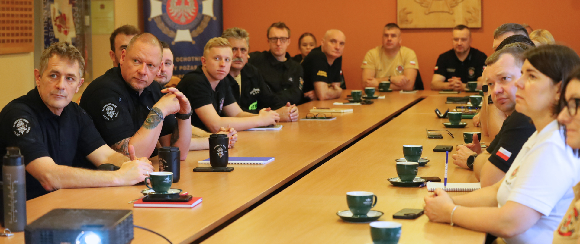 Na zdjęciu widać grupę strażaków siedzących przy stole. 