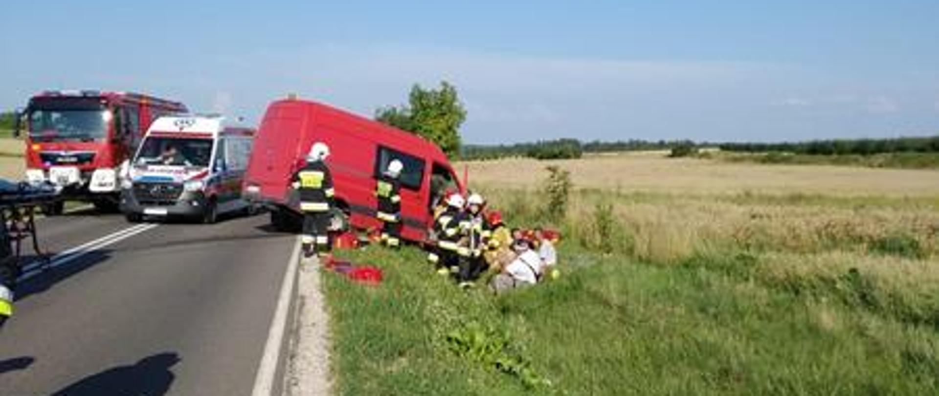 Ratownicy udzielają pomocy osobom poszkodowanym znajdującym się w busie. Pojazd znajduje się częściowo w rowie a częściowo na jezdni.